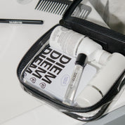 Travel-sized grooming products including bottles and a comb in a black toiletry bag on a white surface.